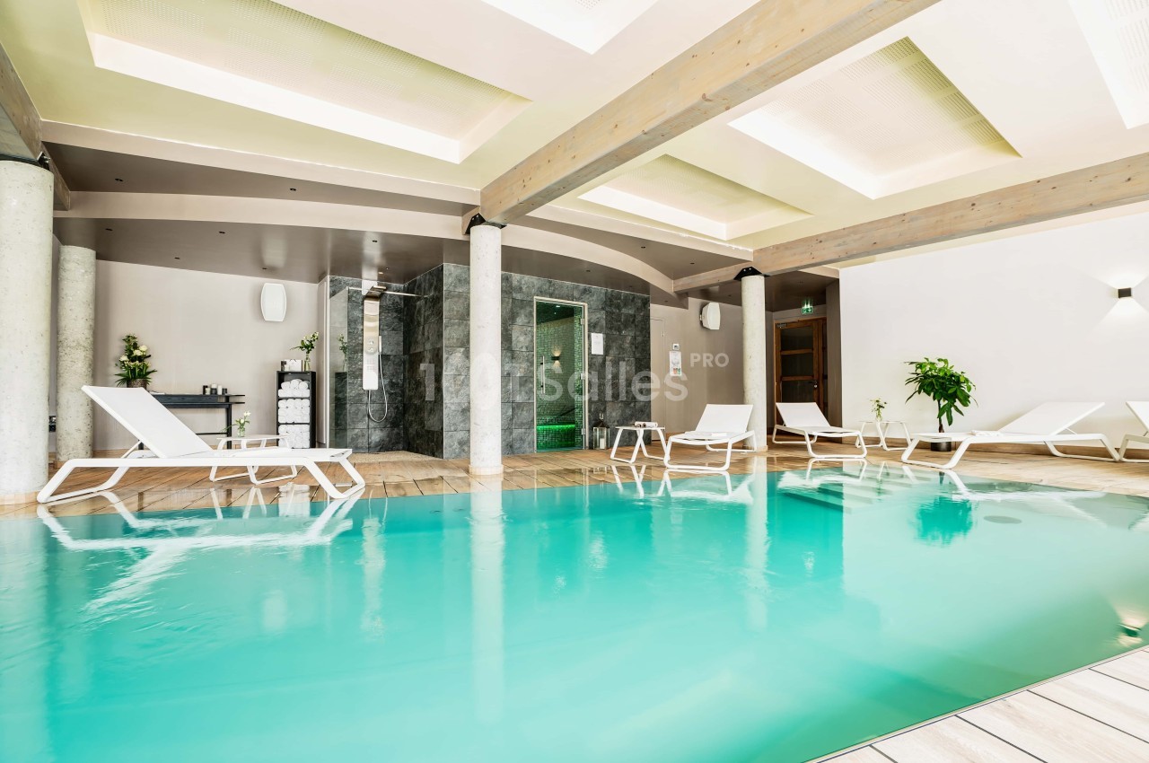 Piscine intérieure avec eau turquoise, entourée de chaises longues blanches et d'une décoration moderne.