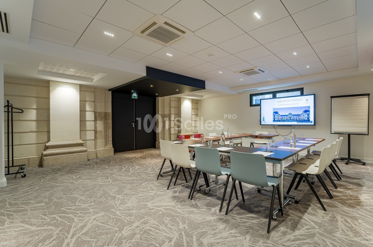 Salle de réunion lumineuse avec table rectangulaire, chaises modernes, écran, paperboard et décorations murales.