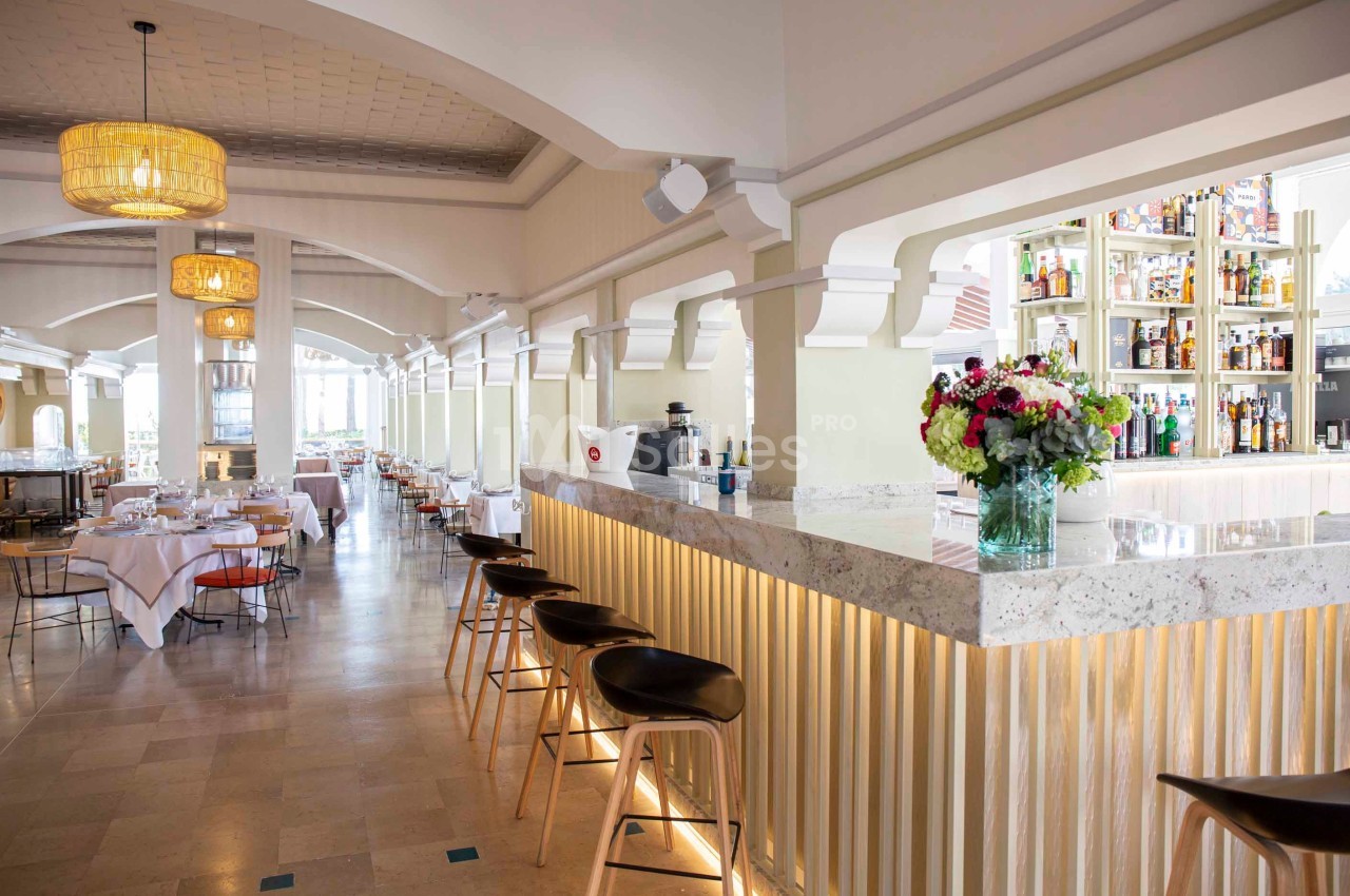 Salle de restaurant lumineuse avec un bar en marbre, des tabourets en bois et des tables dressées en arrière-plan.