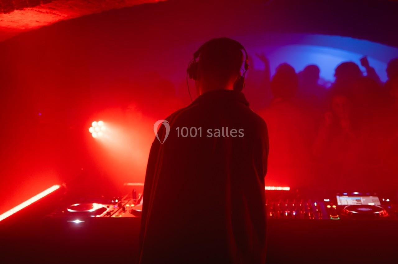 Un DJ mixe de la musique dans une ambiance lumineuse rouge, face à une foule dansante dans un club.