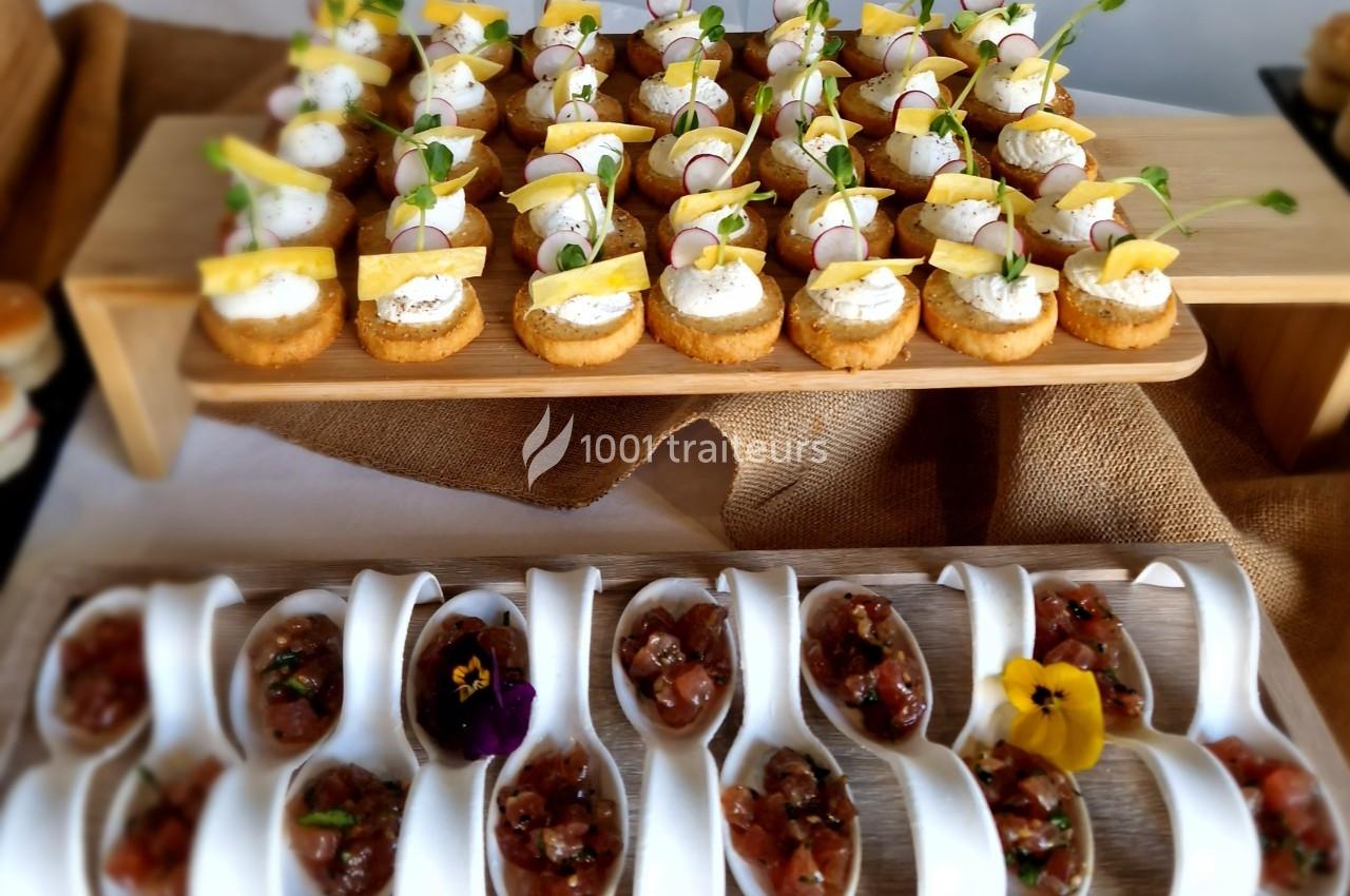 Plateau de bouchées apéritives comprenant des toasts garnis et des cuillères de tartare décorées de fleurs comestibles.