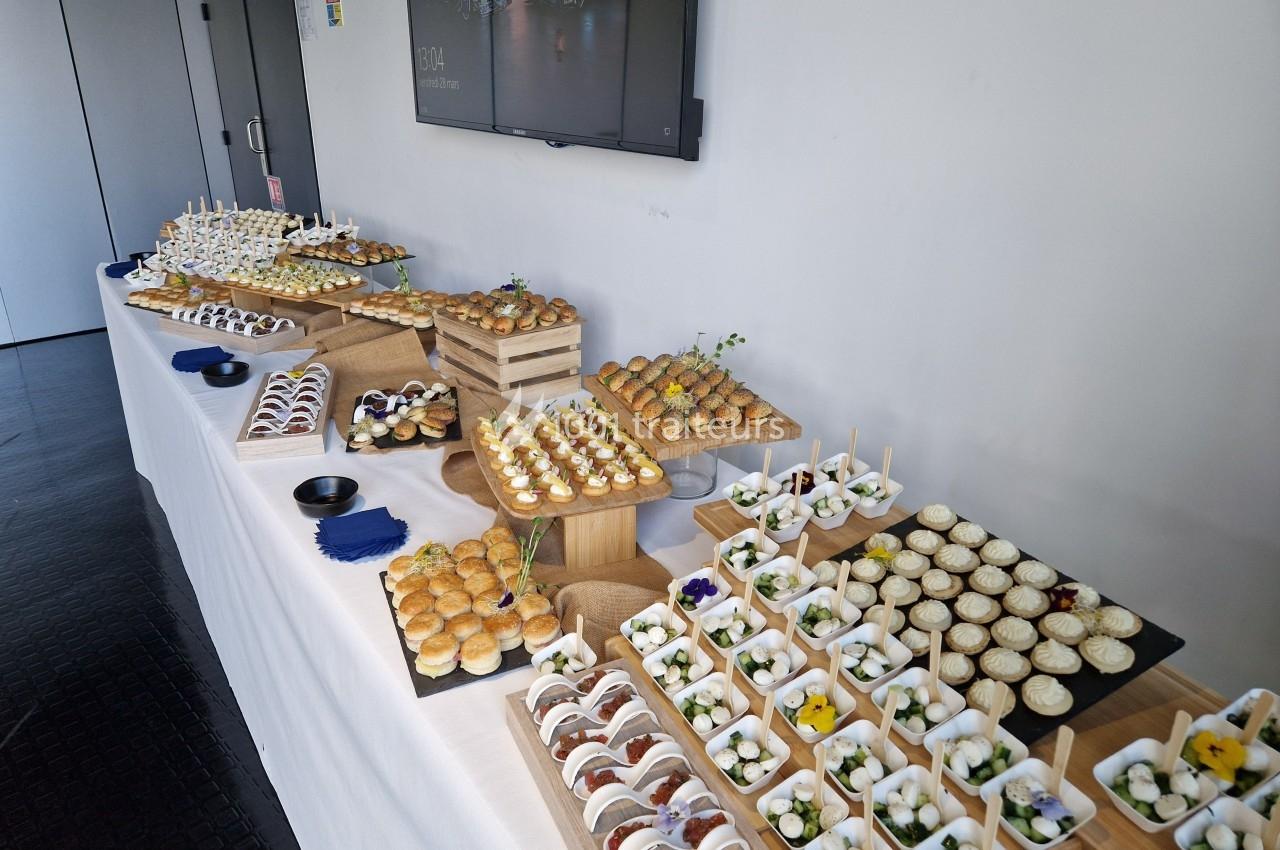Table garnie de divers amuse-bouches et desserts présentés sur des plateaux en bois dans un cadre moderne.