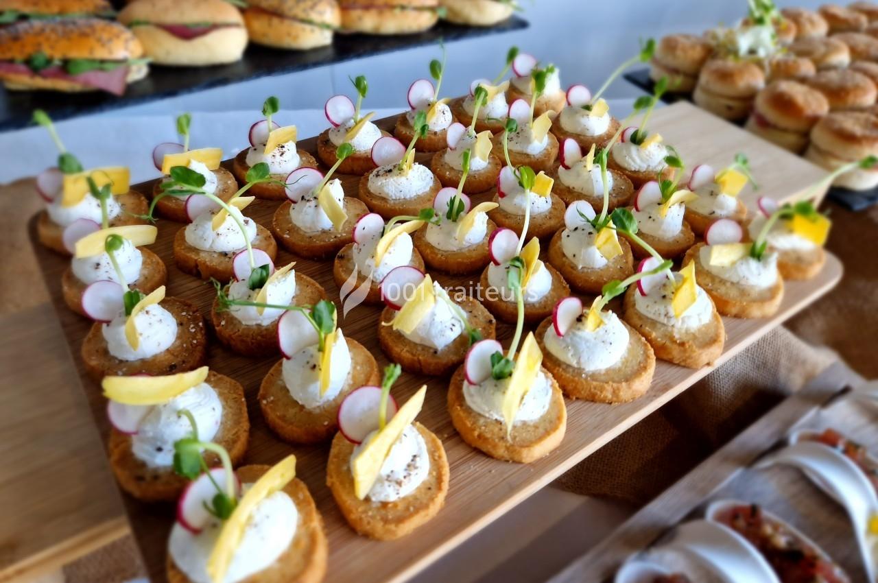Plateau de canapés garnis de fromage frais, radis, pousses vertes et zestes de citron, disposés sur une table.