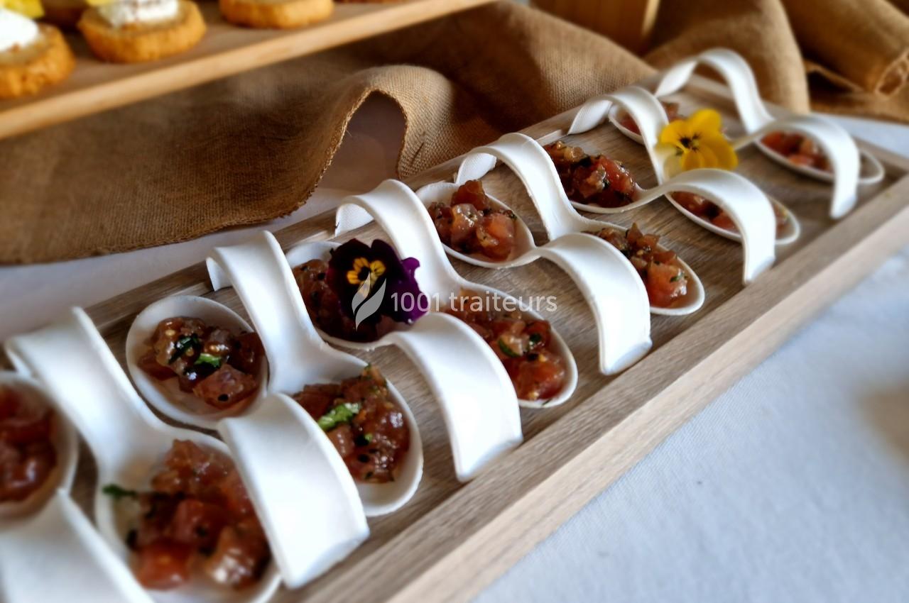 Cuillères en porcelaine contenant des bouchées de tartare, décorées de fleurs comestibles, sur un plateau en bois.
