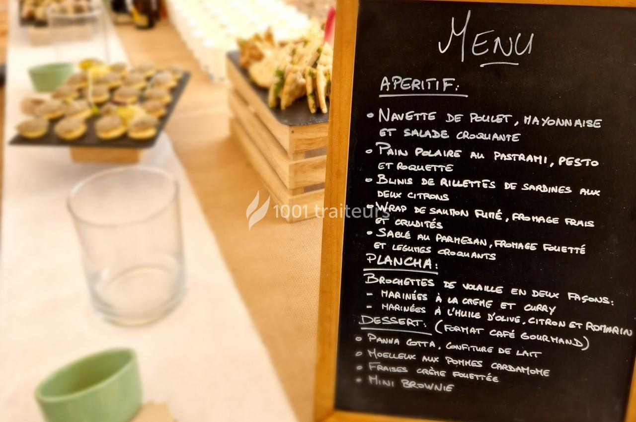 Ardoise affichant un menu écrit à la craie, avec des plats et desserts, sur une table de buffet.