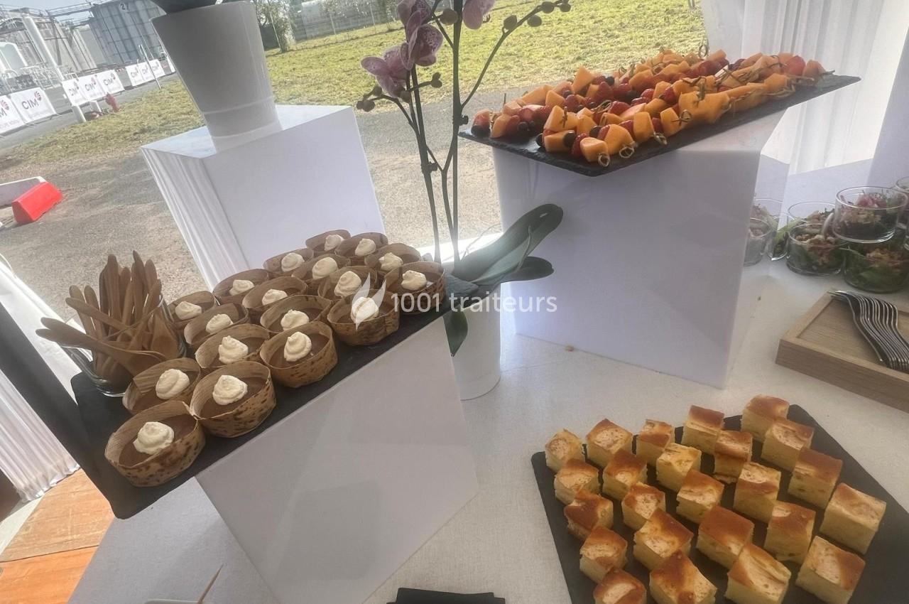 Plateau de desserts et amuse-bouches variés disposés sur des présentoirs blancs lors d'un événement en extérieur.