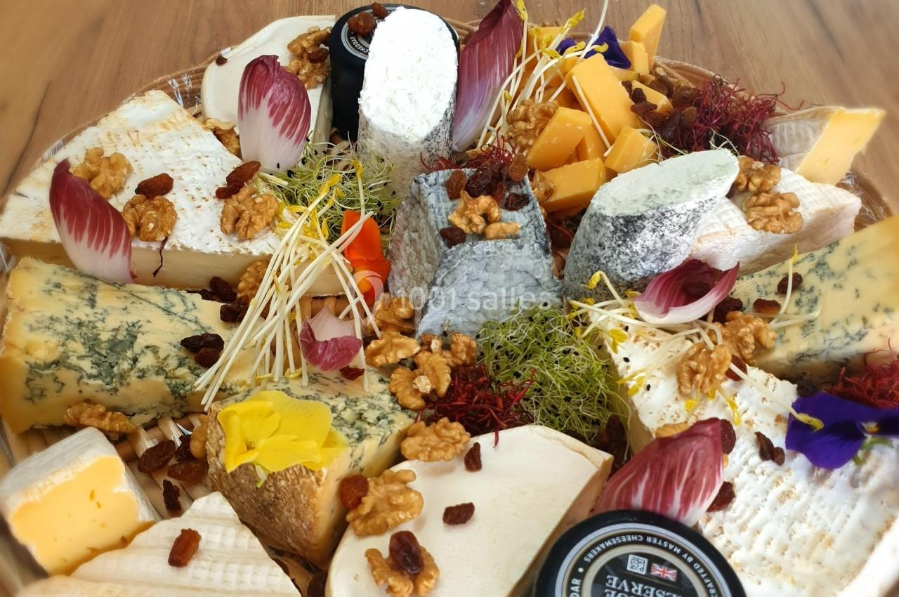 Plateau de fromages variés avec noix, raisins secs, endives, fleurs comestibles et germes, présenté sur un fond en bois.