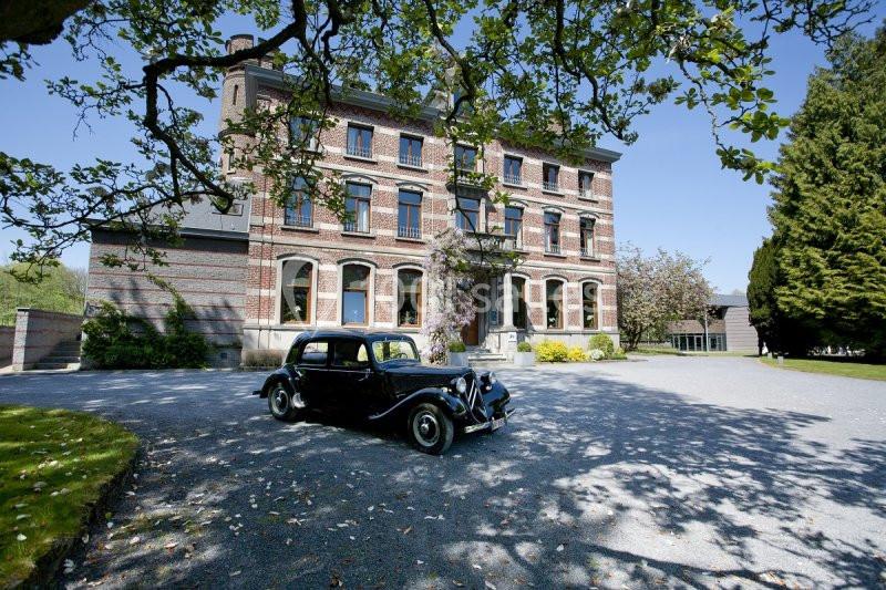 Façade d'un bâtiment en briques rouges avec une voiture ancienne noire stationnée sur une allée gravillonnée.