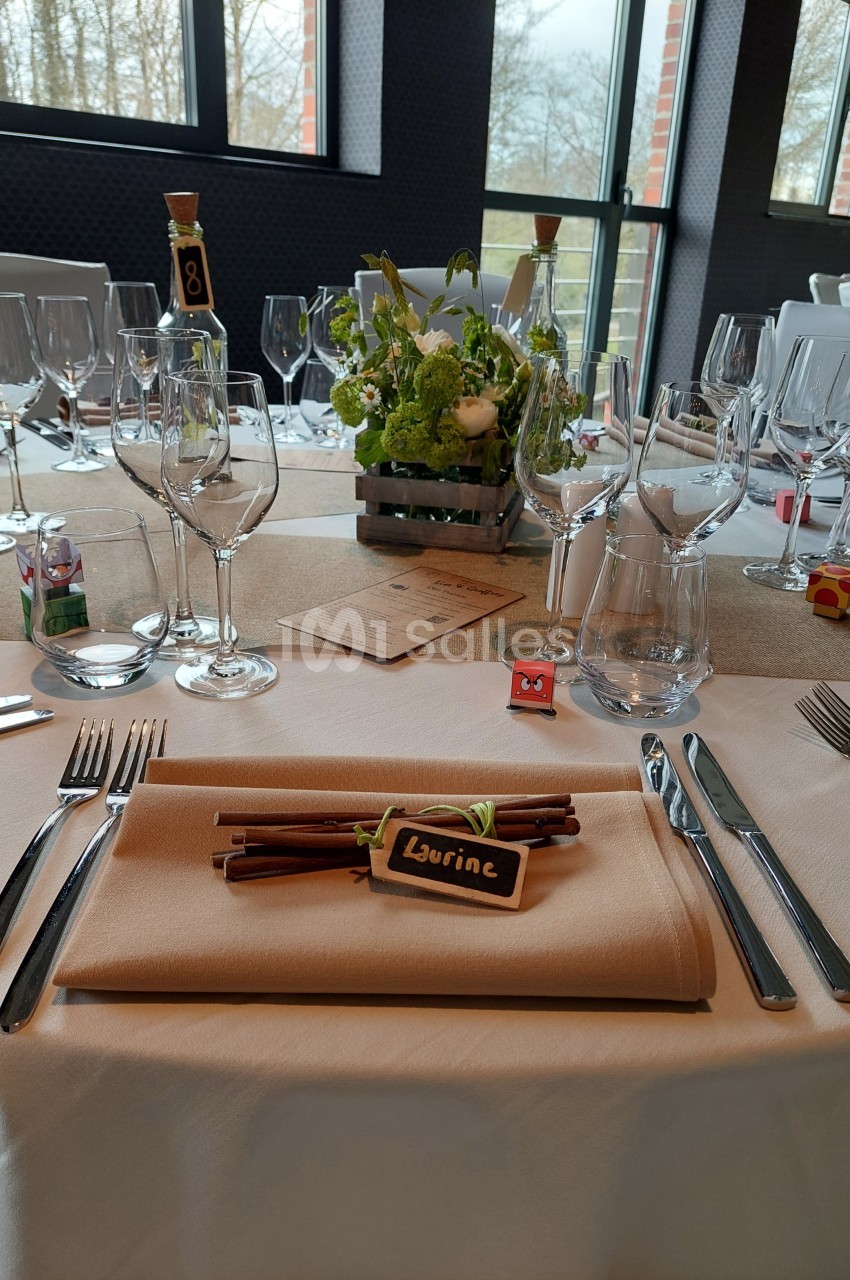 Table élégamment dressée avec serviette beige, couverts, verres et décoration florale au centre.
