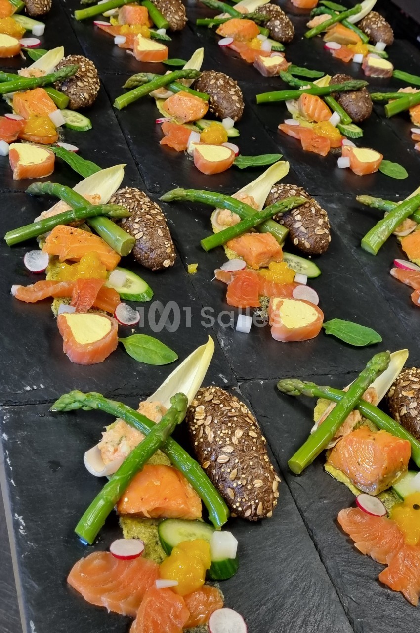 Assiettes dressées avec saumon fumé, asperges vertes, radis, pain aux graines et garnitures colorées sur ardoise noire.