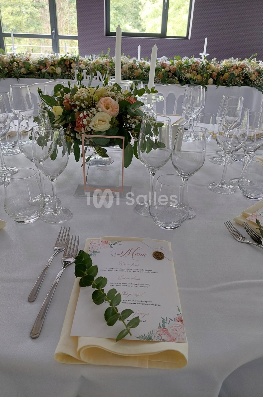 Table de réception élégamment dressée avec des fleurs, des bougies, des verres et un menu décoré de motifs floraux.