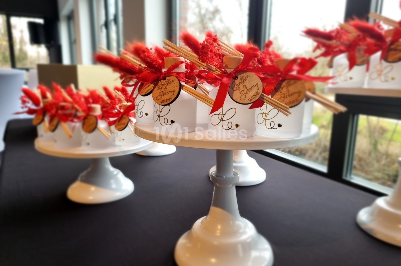 Présentoirs blancs décorés de bouquets rouges et étiquettes en bois, disposés sur une table près d'une fenêtre.