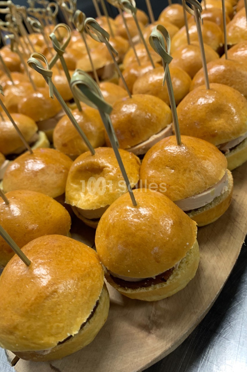 Mini-burgers dorés garnis, présentés sur un plateau en bois avec des pics en bambou.