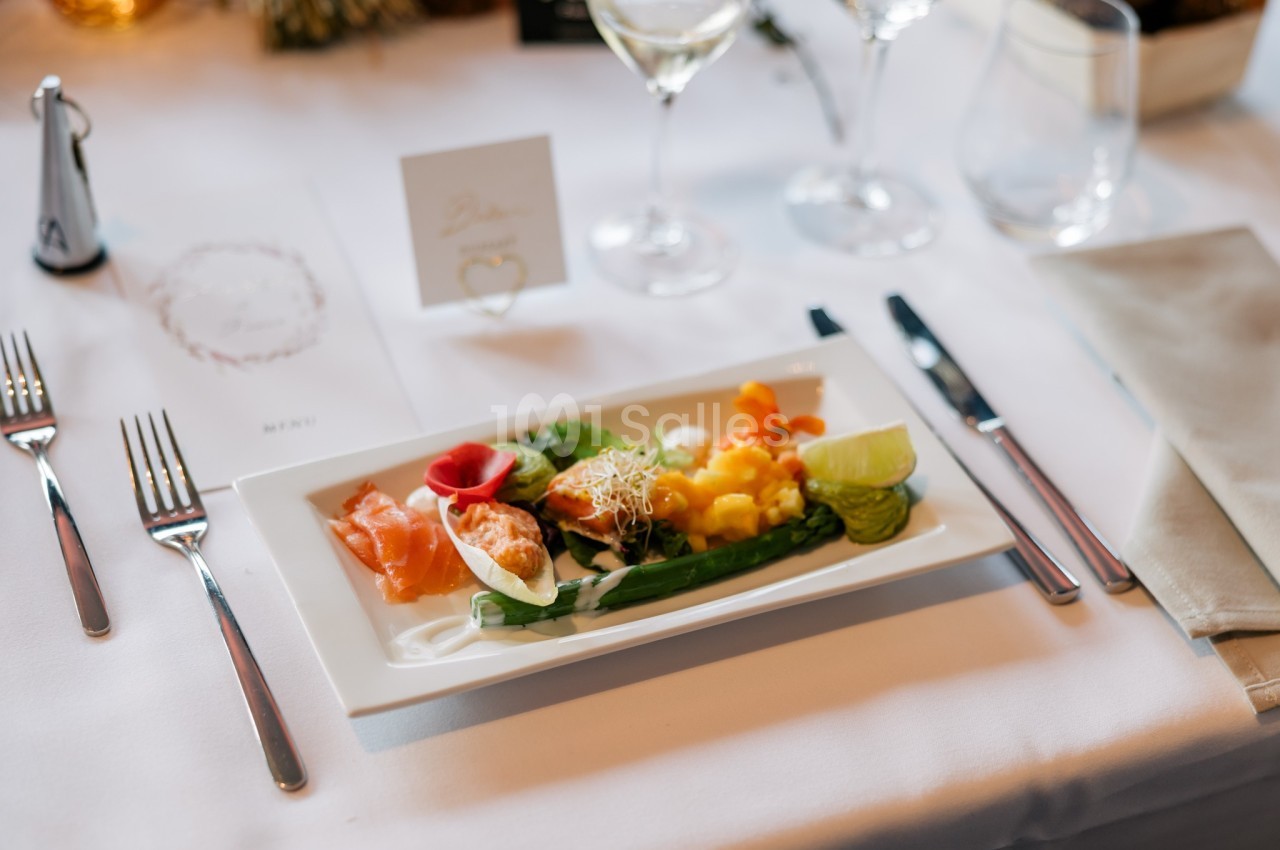 Assiette de mets variés avec saumon fumé, légumes et citron, servie sur une table dressée avec couverts et verres.