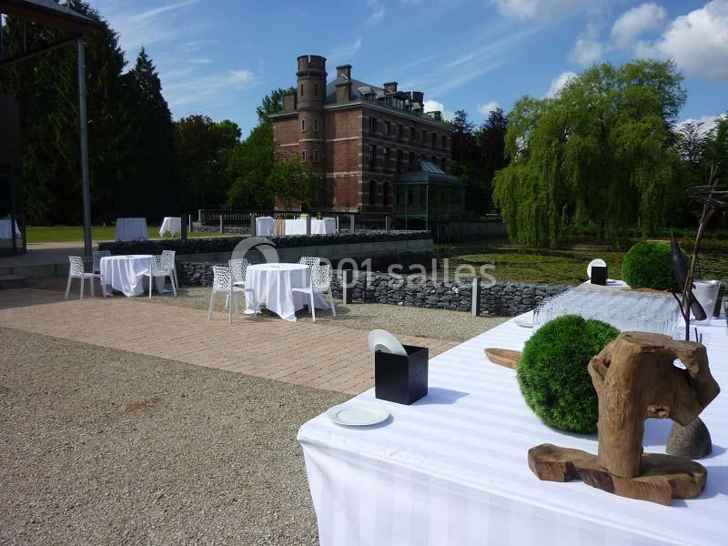 Tables dressées en extérieur près d'un étang, avec un château en arrière-plan sous un ciel dégagé.