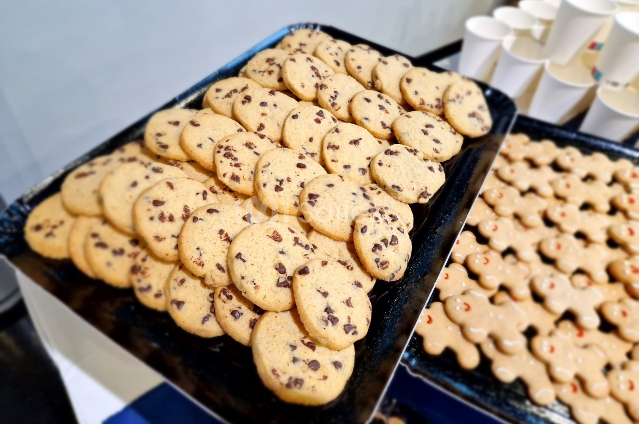 Plateau de biscuits aux pépites de chocolat et de biscuits en forme de bonhommes, disposés près de gobelets blancs.