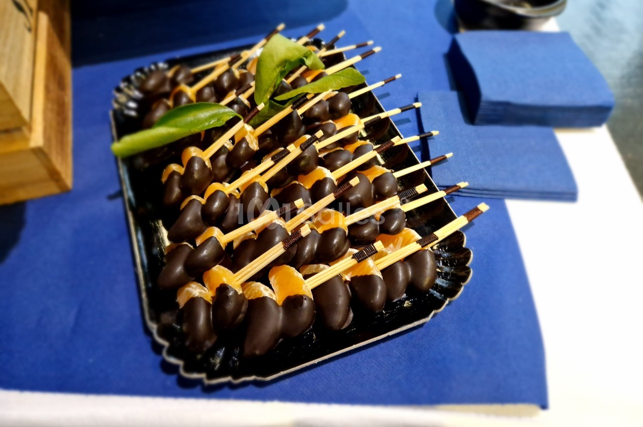 Plateau de brochettes de fruits enrobés de chocolat, présenté sur une nappe bleue avec des serviettes assorties.
