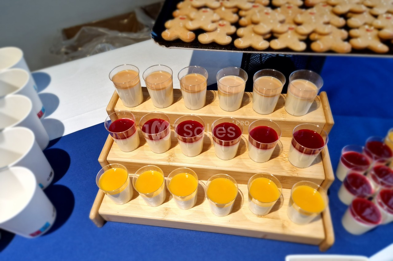 Plateau en bois présentant des verrines colorées alignées, avec des biscuits en arrière-plan sur une table bleue.