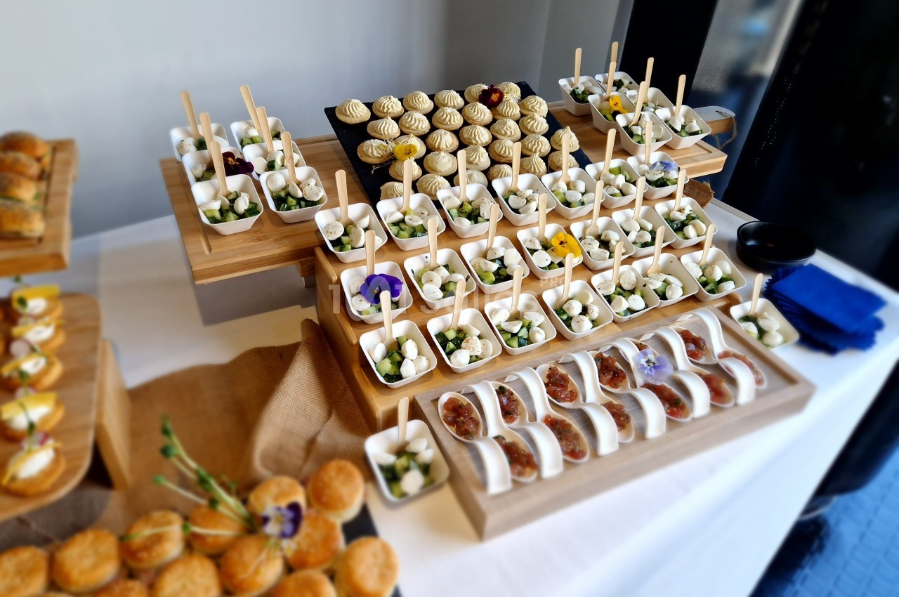 Plateau de buffet avec des amuse-bouches variés, disposés sur des présentoirs en bois, incluant brochettes et mini…