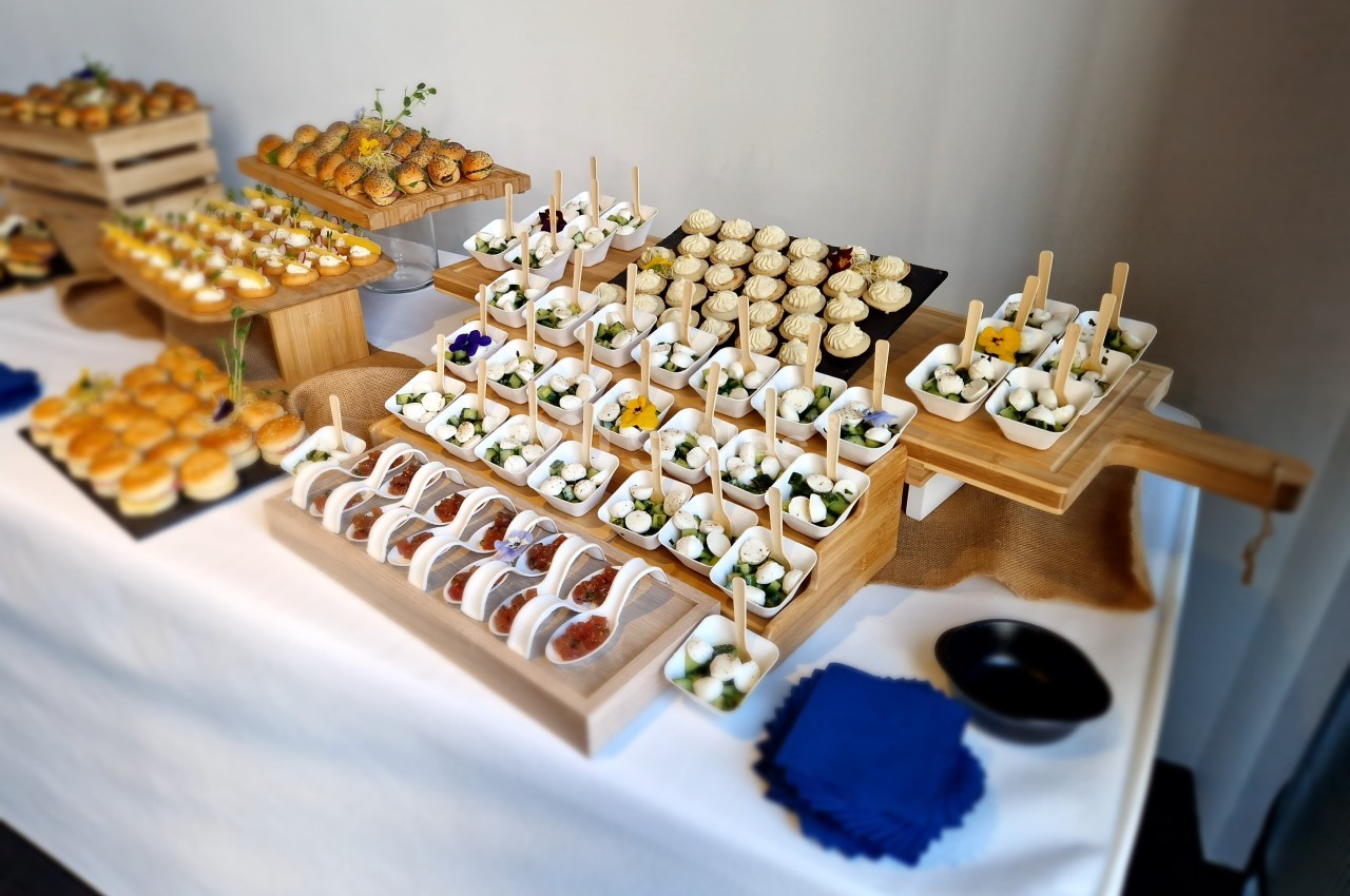 Buffet de petites bouchées salées et sucrées présentées sur des plateaux en bois, disposés sur une nappe blanche.