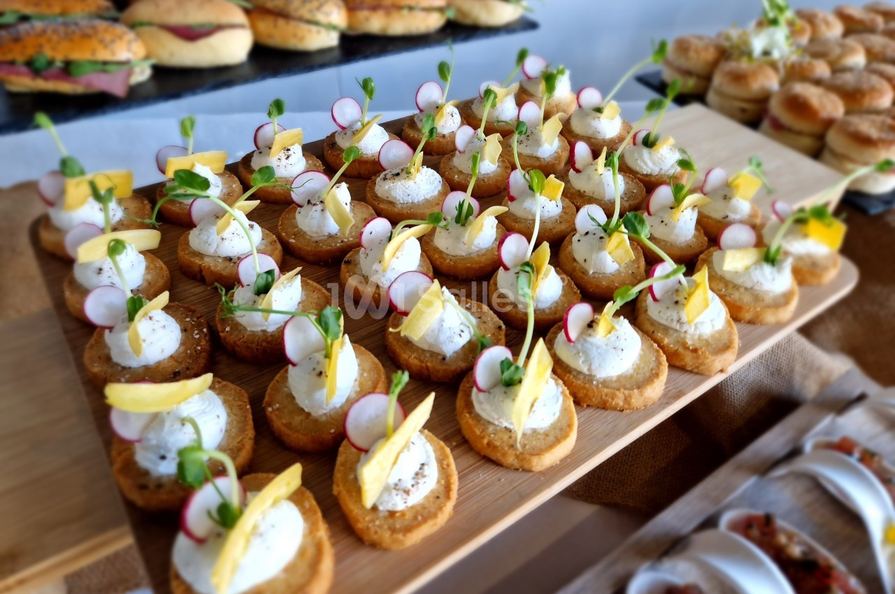 Plateau de canapés garnis de fromage frais, radis, pousses vertes et zestes de citron, disposés sur une table.