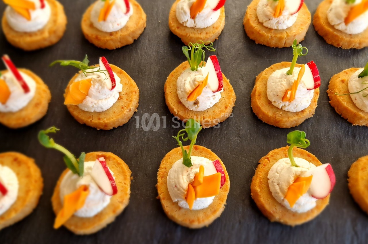 Assortiment de canapés sur une ardoise, garnis de crème et décorés de légumes colorés.