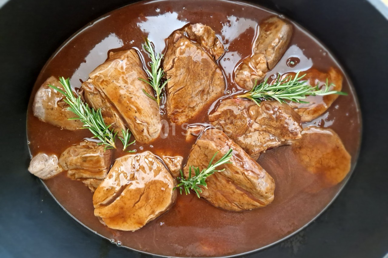 Morceaux de viande mijotés dans une sauce brune, garnis de brins de romarin, présentés dans une cocotte noire.