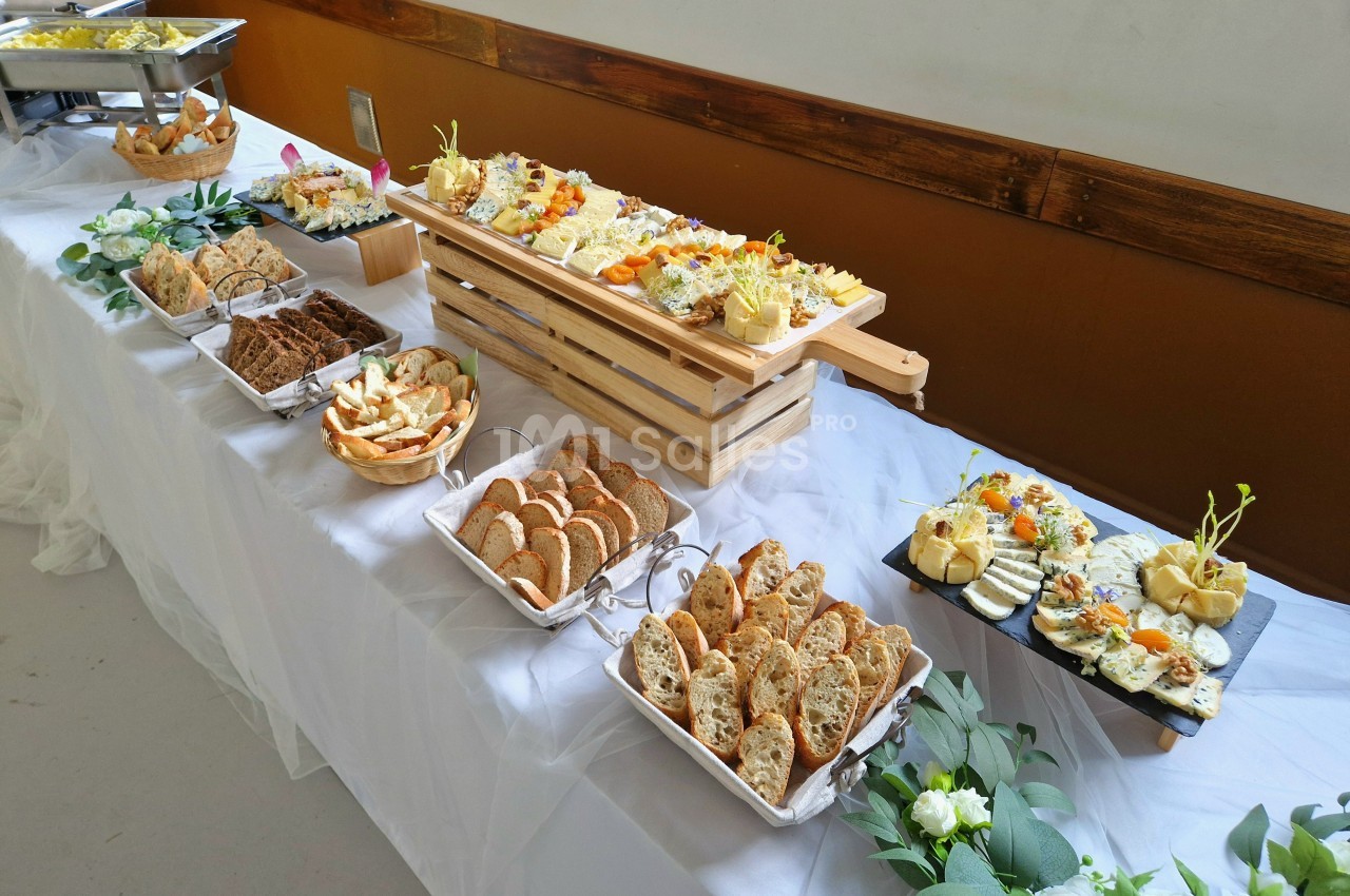 Buffet avec divers plats froids, pains, fromages et décorations florales sur une table blanche.