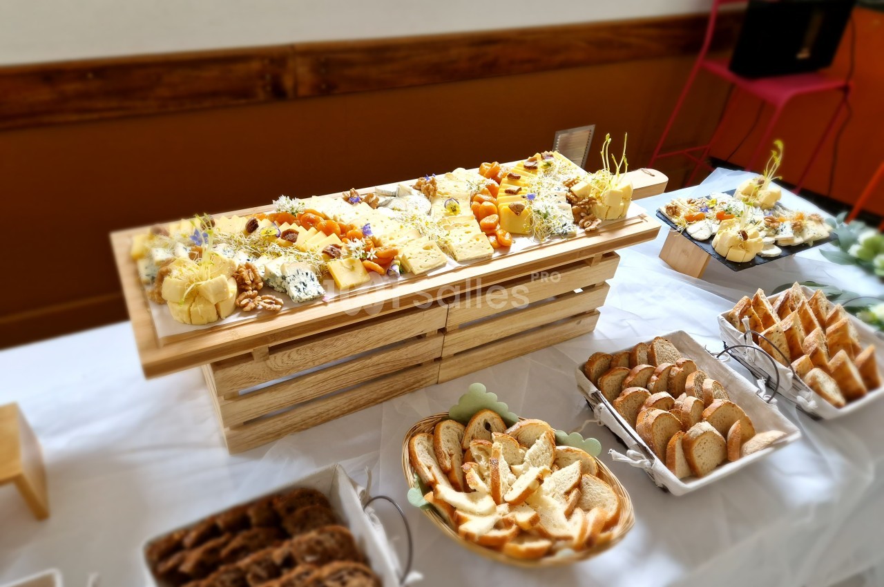 Plateau de fromages variés avec fruits secs et pain tranché disposé sur une table blanche pour un buffet.