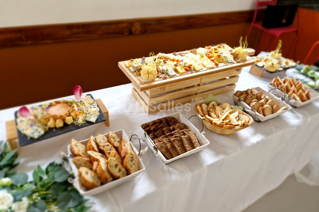 Table dressée avec un buffet de fromages variés, pains et accompagnements, disposés sur des plateaux et nappes blanches.