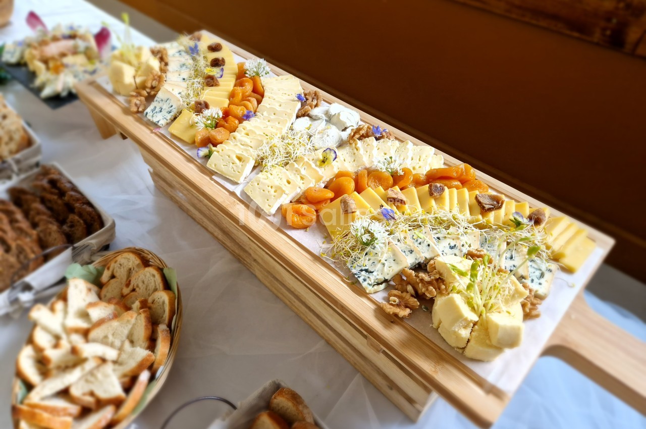Plateau de fromages variés avec fruits secs, noix et herbes, accompagné de pains et viennoiseries sur une table.
