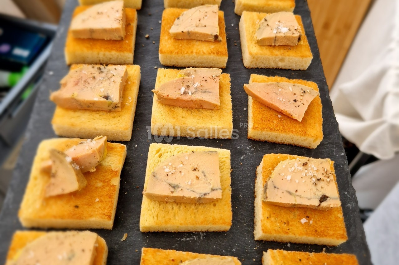 Tranches de foie gras posées sur des toasts dorés, disposés sur une ardoise noire.