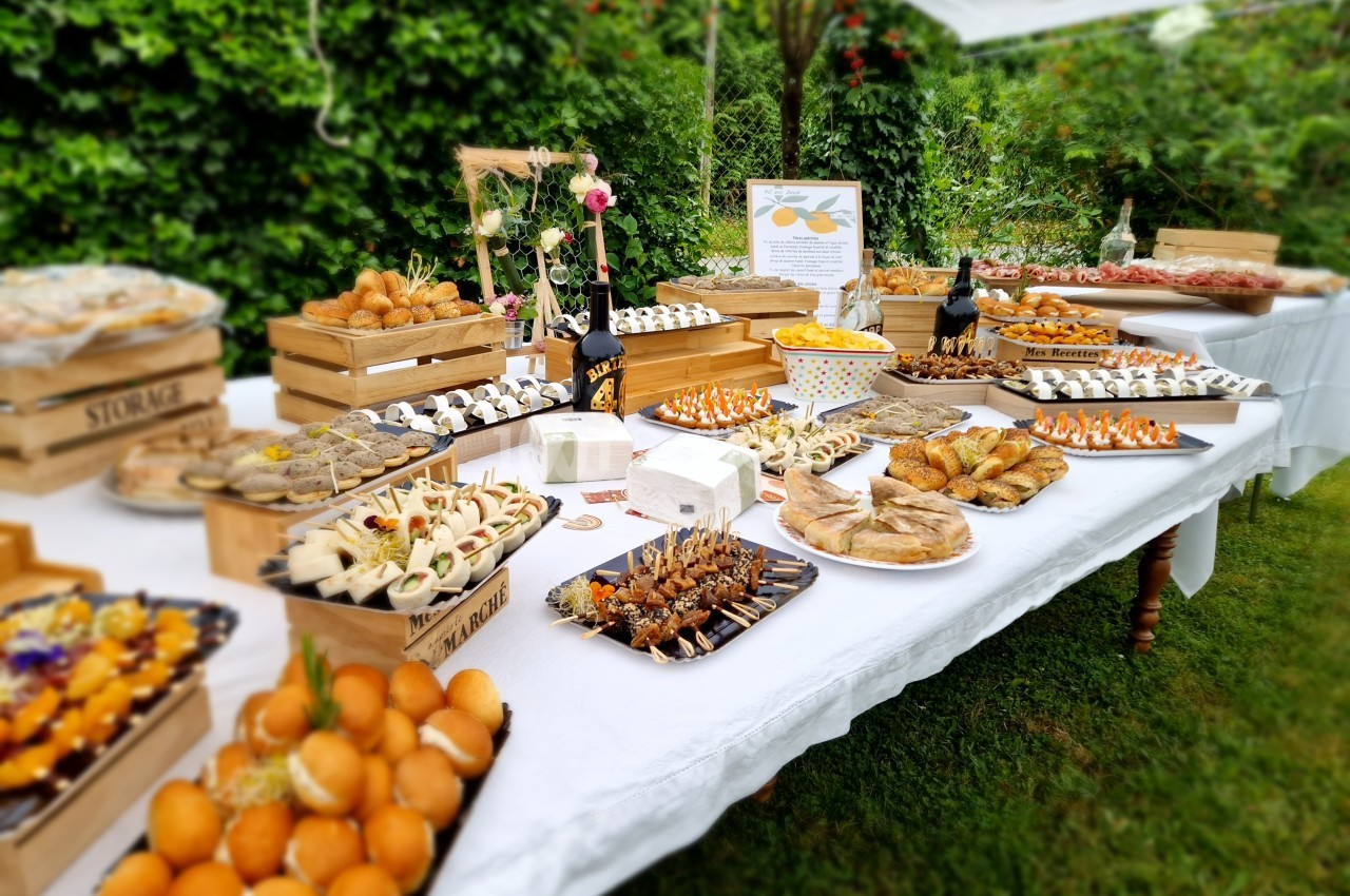 Table garnie de divers plats et amuse-bouches disposés sur des plateaux en bois, dans un jardin verdoyant.