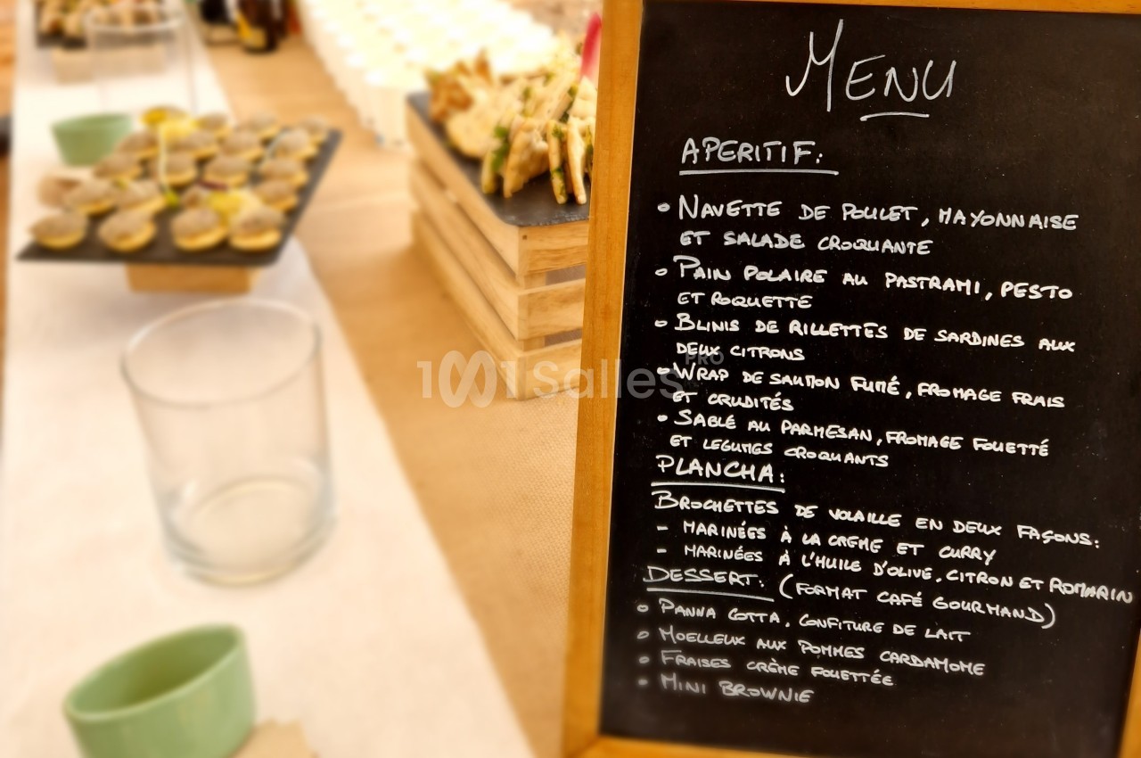 Ardoise affichant un menu écrit à la craie, avec des plats et desserts, sur une table de buffet.