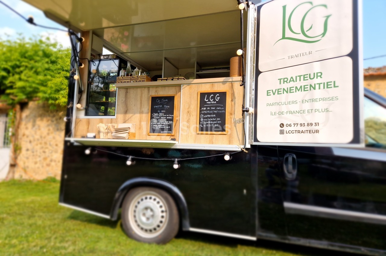 Camion traiteur noir avec comptoir en bois, ardoises de menu et enseigne ’Traiteur événementiel’.