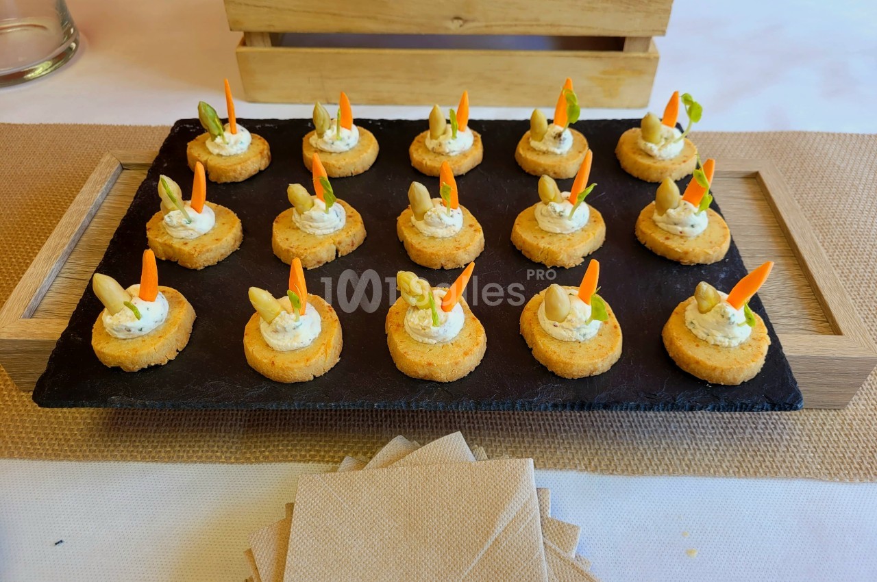 Plateau d'amuse-bouches sur ardoise, garnis de crème et décorés de légumes, présenté sur une table avec serviettes.