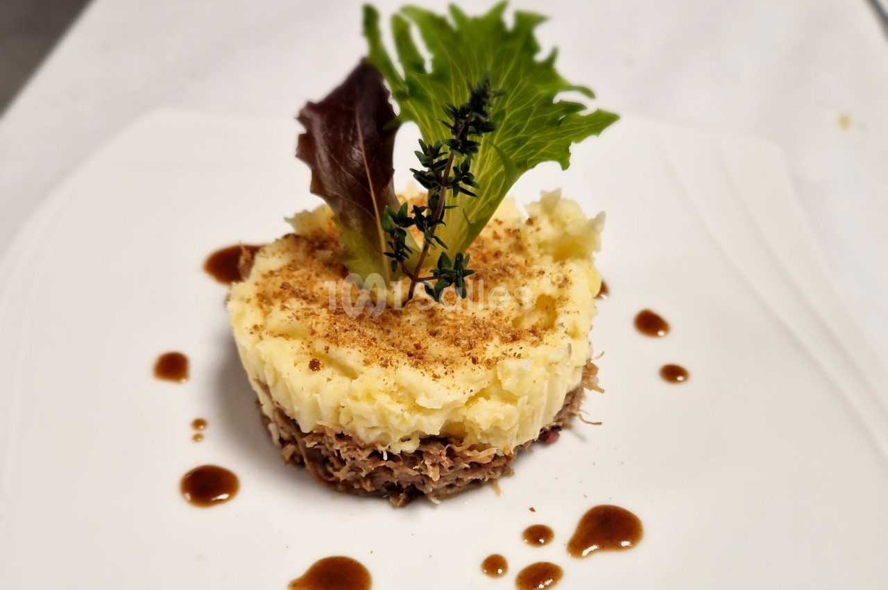 Plat dressé avec une base de viande effilochée, purée de pommes de terre, feuilles de salade et sauce en décoration.