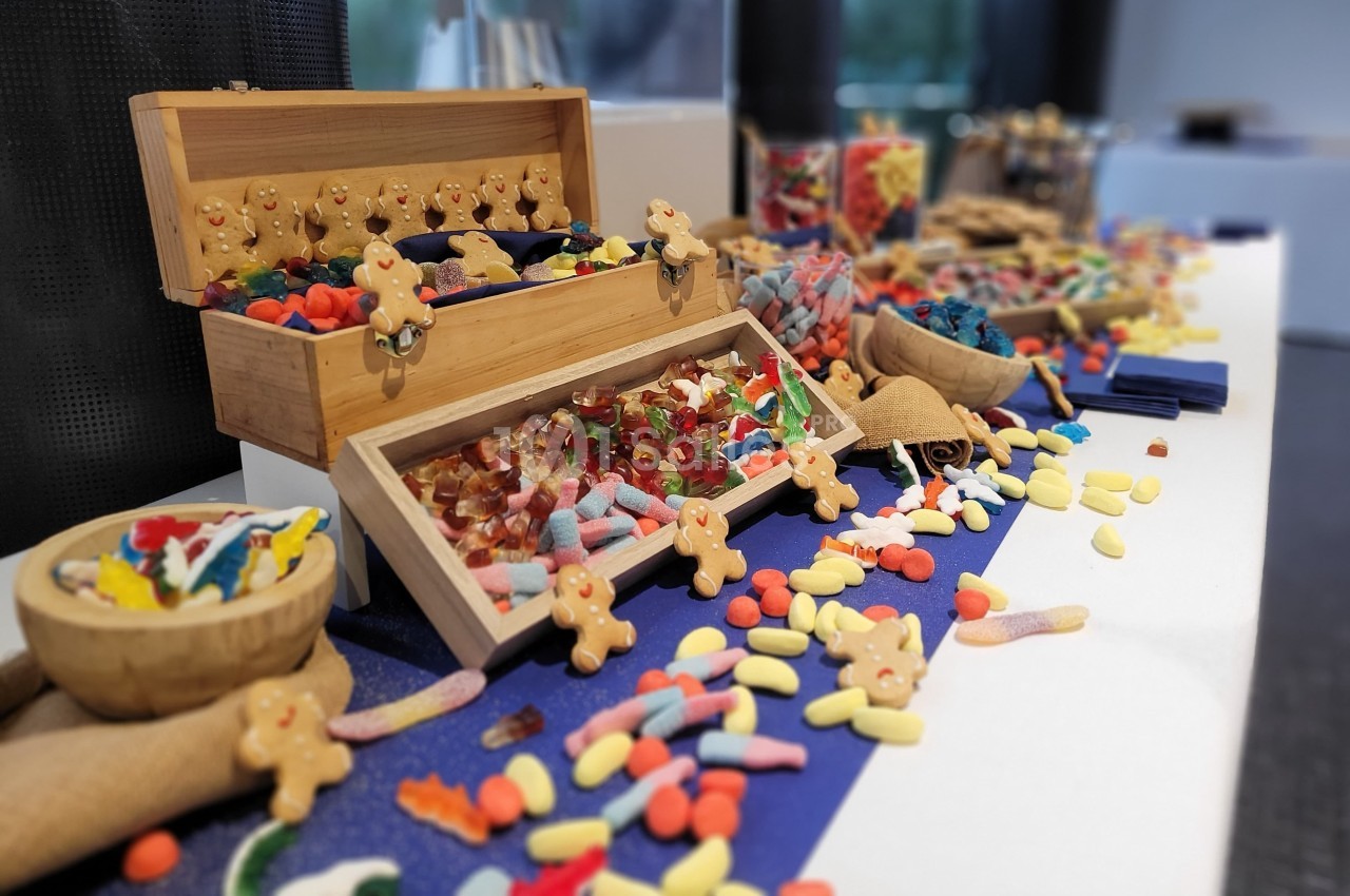 Buffet coloré de bonbons variés, avec des boîtes en bois ouvertes et des friandises répandues sur une nappe bleue.
