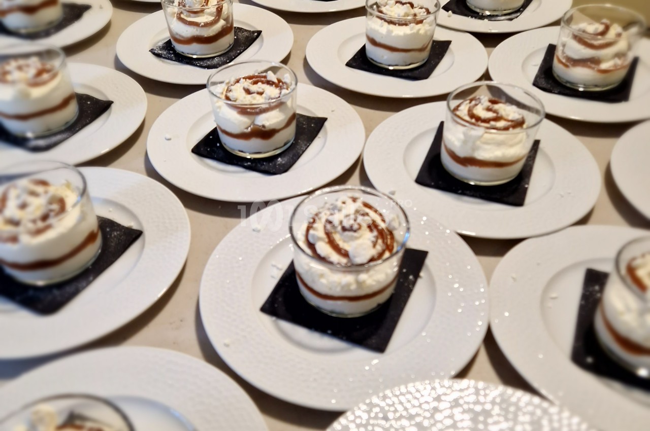 Desserts individuels en verrines avec crème et caramel, présentés sur des assiettes blanches avec des sous-verres noirs.