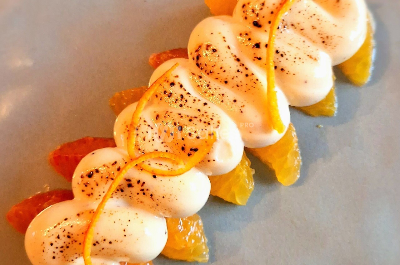 Dessert composé de segments d'agrumes et de crème légèrement caramélisée, décoré de zestes d'orange.