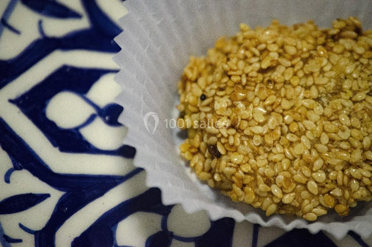Confiserie enrobée de graines de sésame présentée dans une caissette en papier sur un fond de motifs bleus.