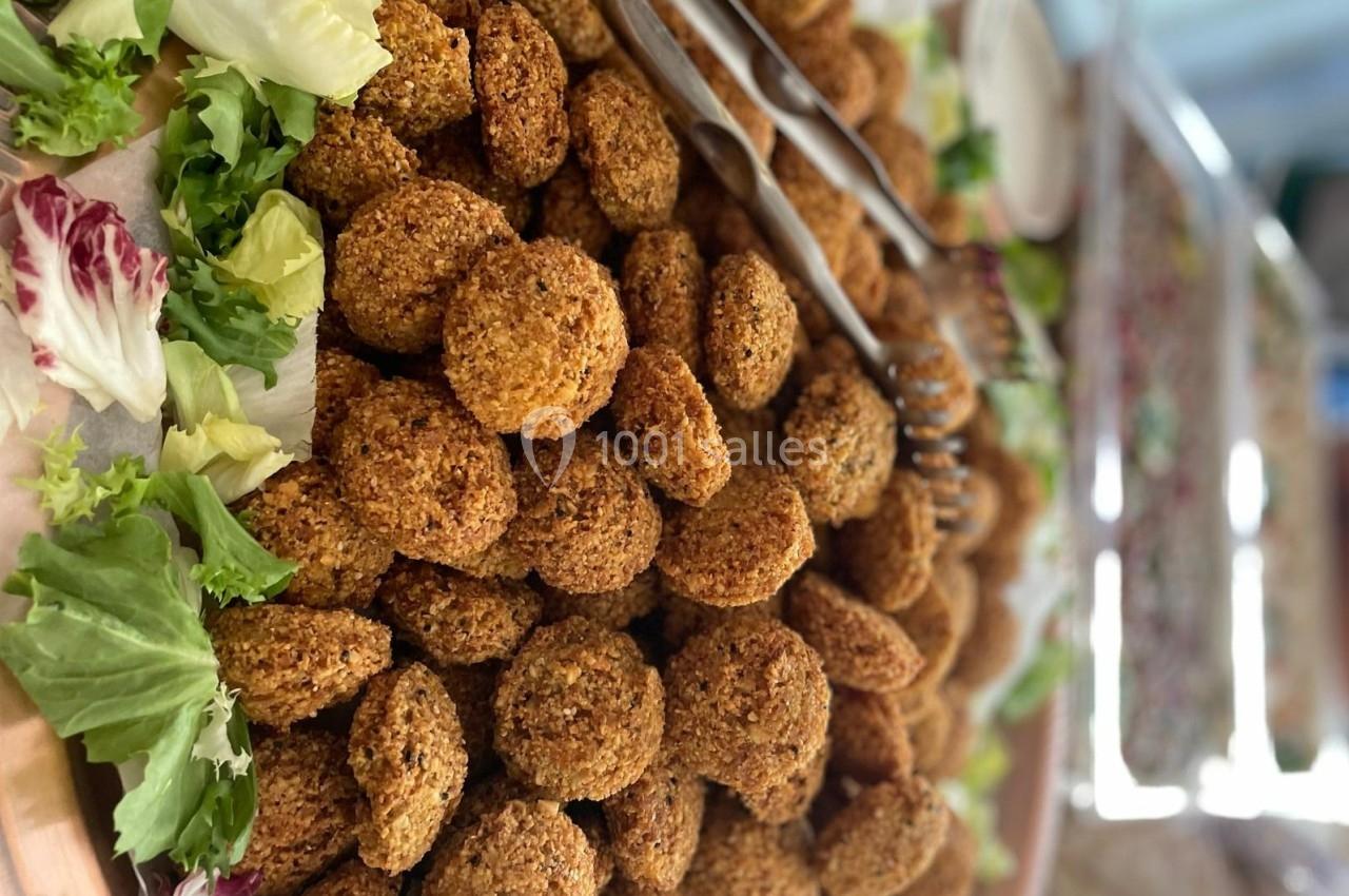 Assiette garnie de falafels dorés entourés de feuilles de salade et accompagnée de pinces en métal.
