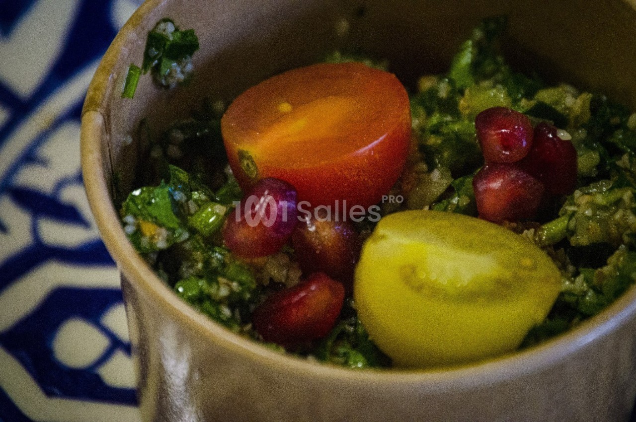 Salade taboulé garnie de tomates cerises et graines de grenade, servie dans un bol sur une nappe à motifs bleus.