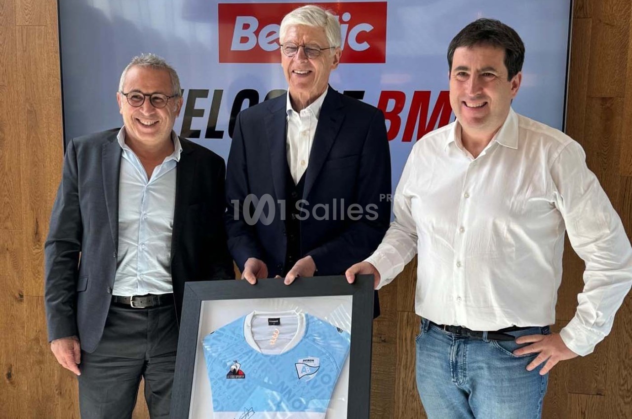Trois hommes posent debout avec un maillot de sport encadré devant un écran affichant ’Beetic’.