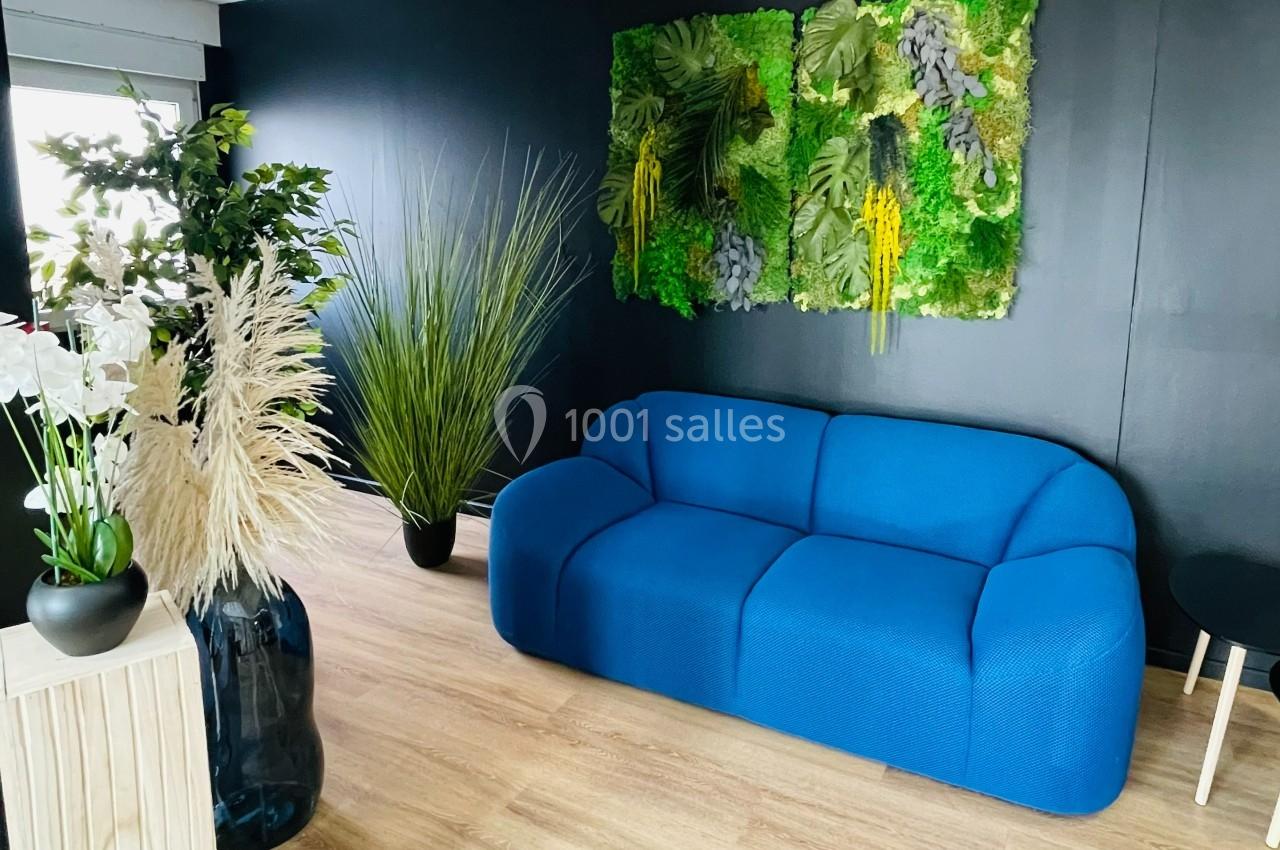 Canapé bleu dans un salon moderne avec mur noir, décoration végétale murale et plantes en pots sur sol en bois clair.