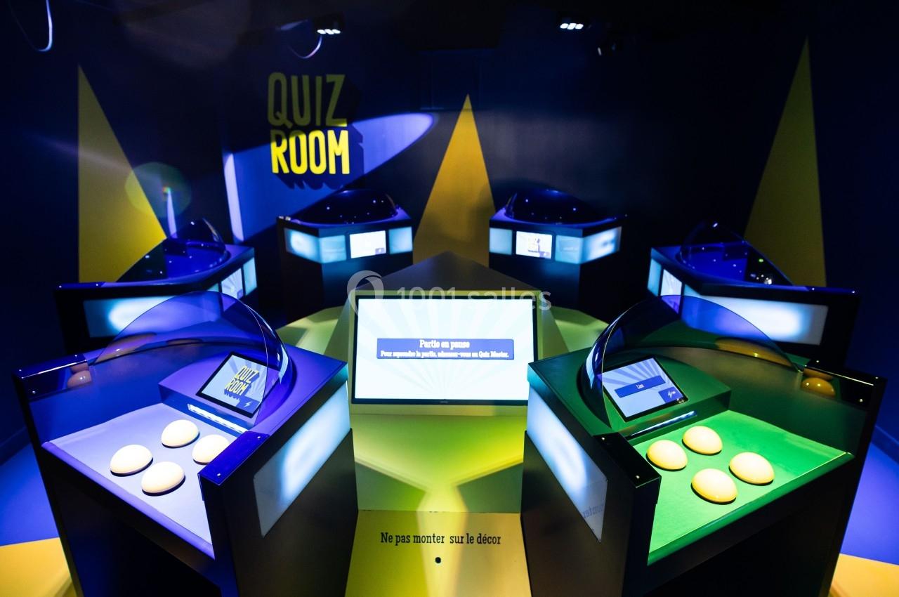Salle de quiz interactive avec plusieurs pupitres lumineux équipés d'écrans et de boutons colorés.