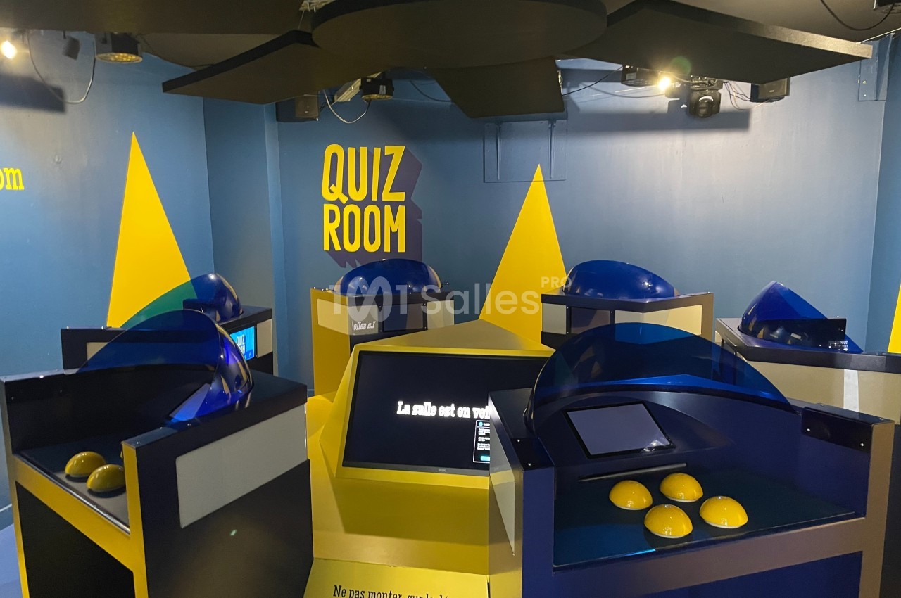 Salle de quiz interactive avec plusieurs bornes équipées d'écrans tactiles et de buzzers jaunes.