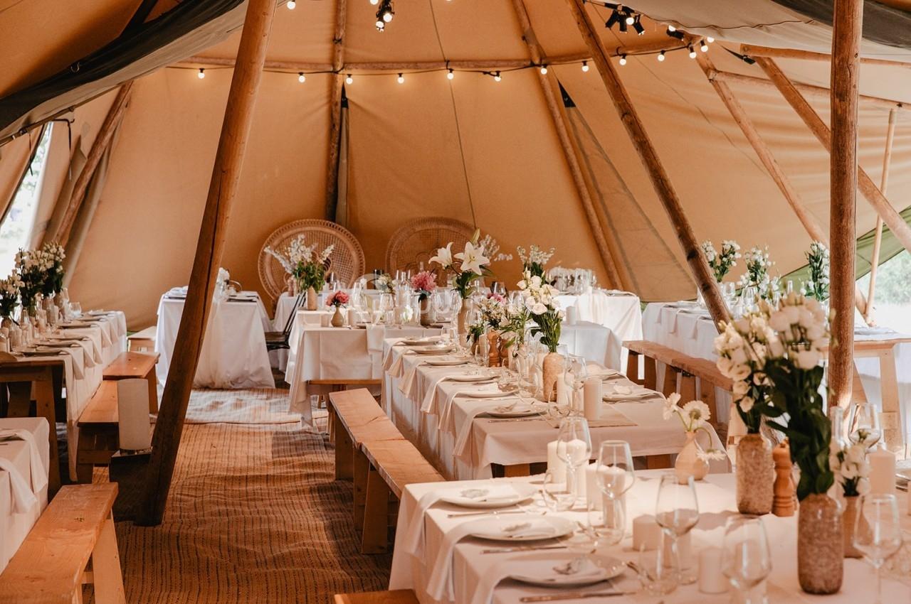 Intérieur d'une tente décorée pour un événement, avec tables dressées, nappes blanches et arrangements floraux.