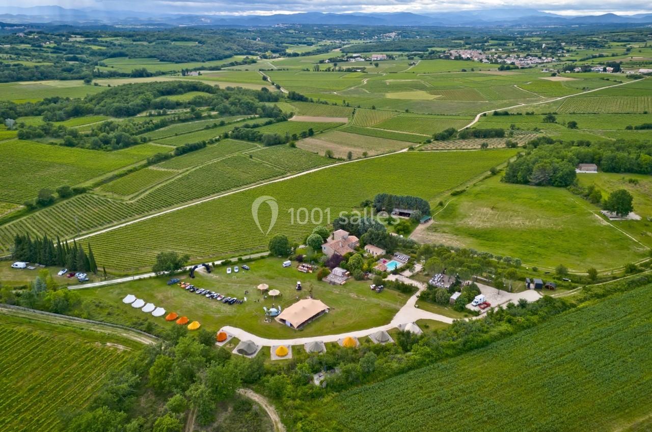 Vue aérienne d'un domaine rural avec des bâtiments, des tentes et des champs verdoyants environnants.