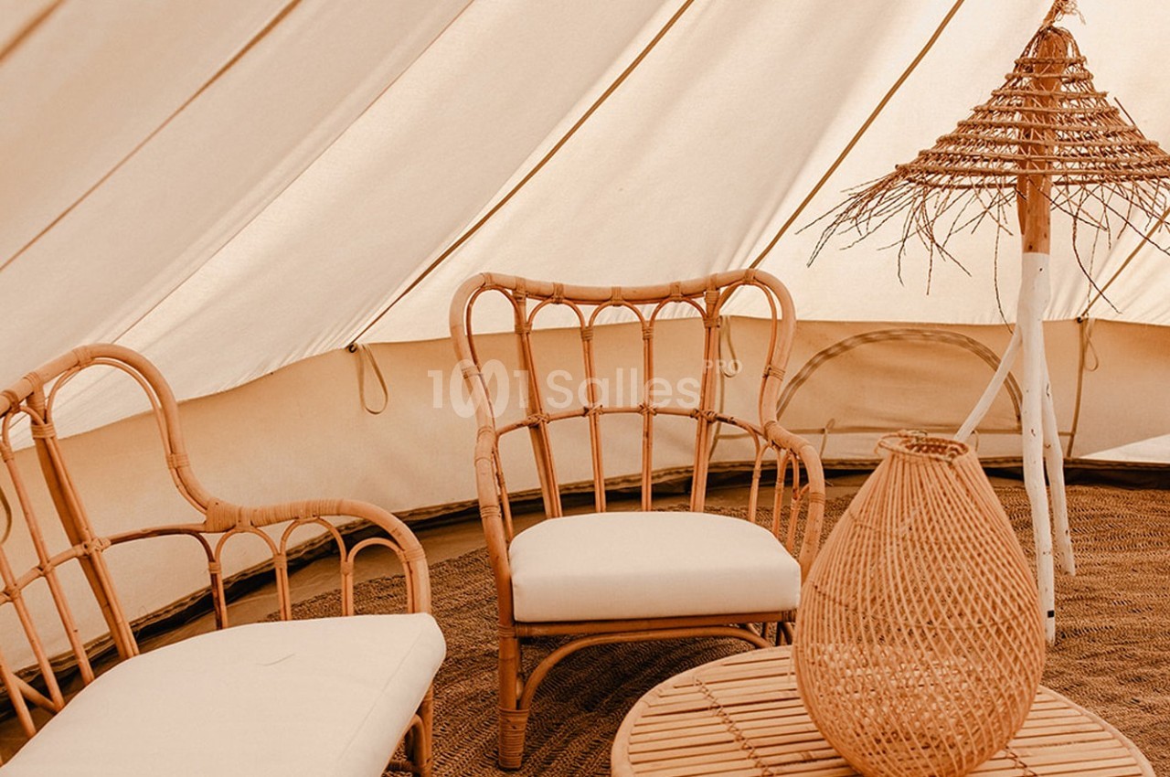 Mobilier en rotin avec coussins blancs dans une tente beige, éclairée par une lumière douce.